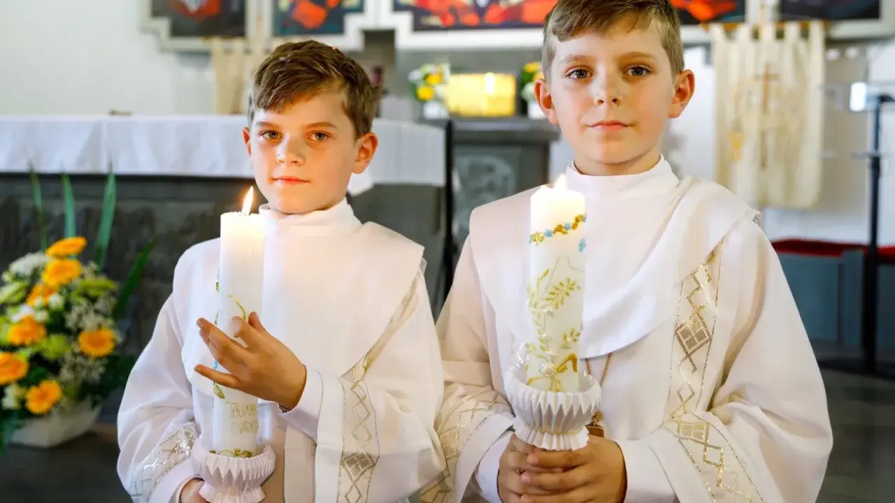 Dwóch chłopców w albach trzyma zapalone świece. Czy do komunii potrzebna jest świeca? Tak, symbolizuje światło Chrystusa.