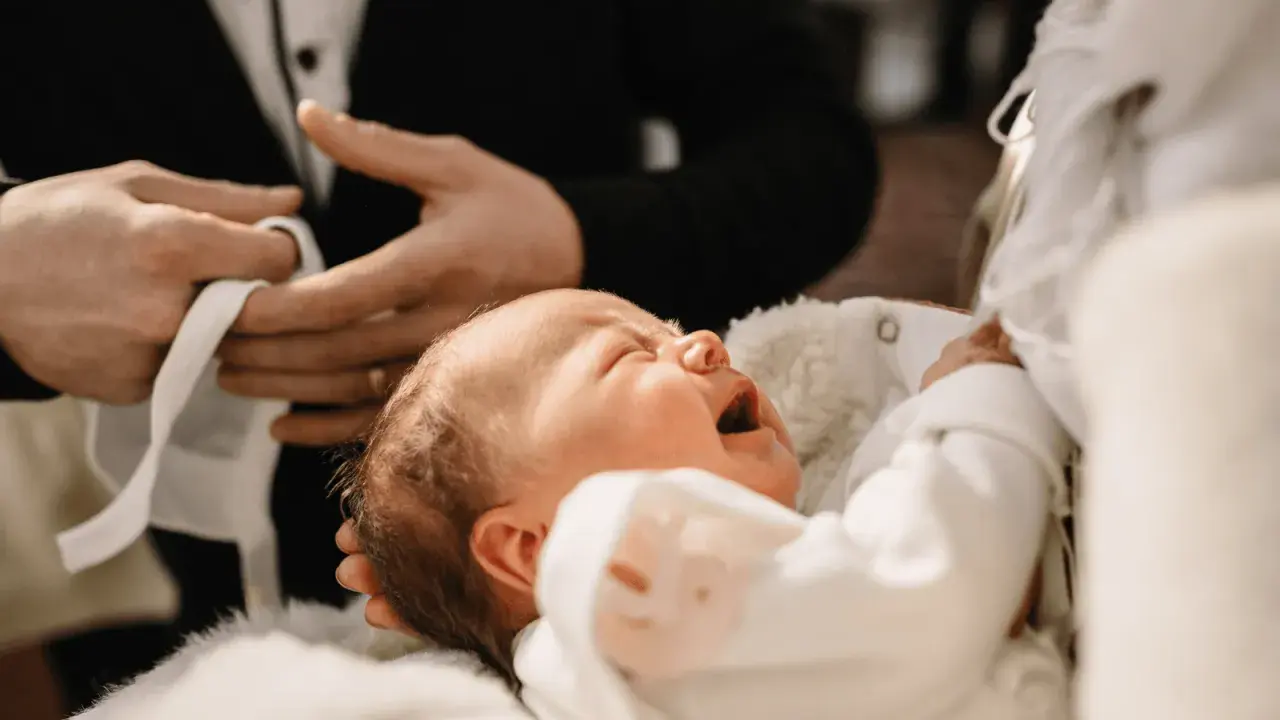 Płacz dziecka podczas chrztu krok po kroku. Dziecko w białej szatce, trzymane przez rodziców.