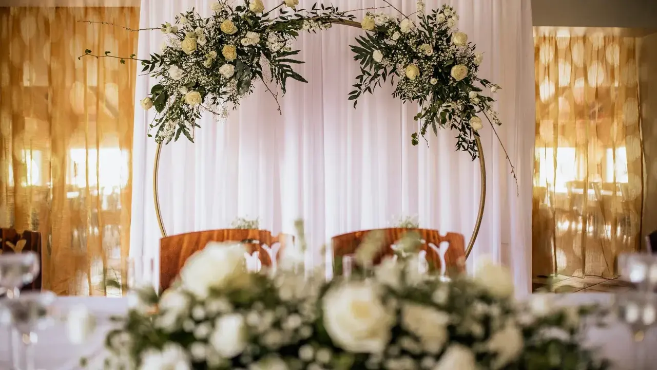 Elegancki ołtarz na ślub w plenerze, ozdobiony białymi kwiatami i zielenią na złotym okręgu.