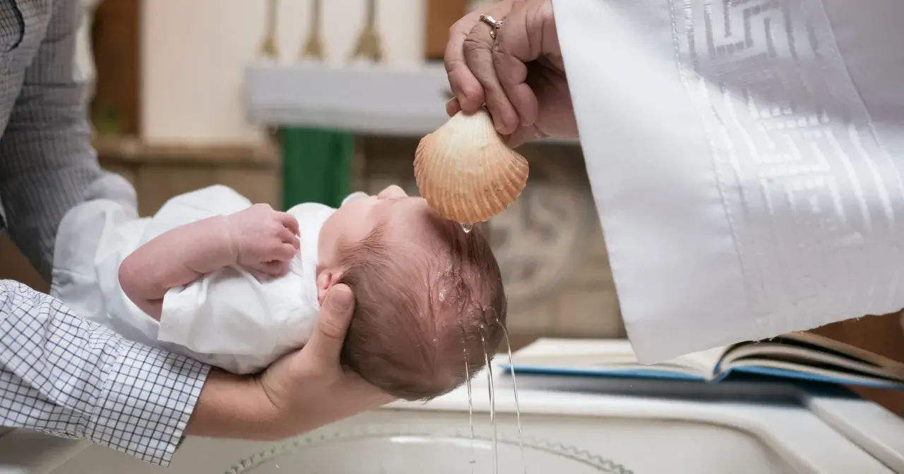 Chrzest dziecka. Kapłan polewa główkę niemowlęcia wodą święconą z muszli. To ważny moment, jak ile daje się na chrzciny.