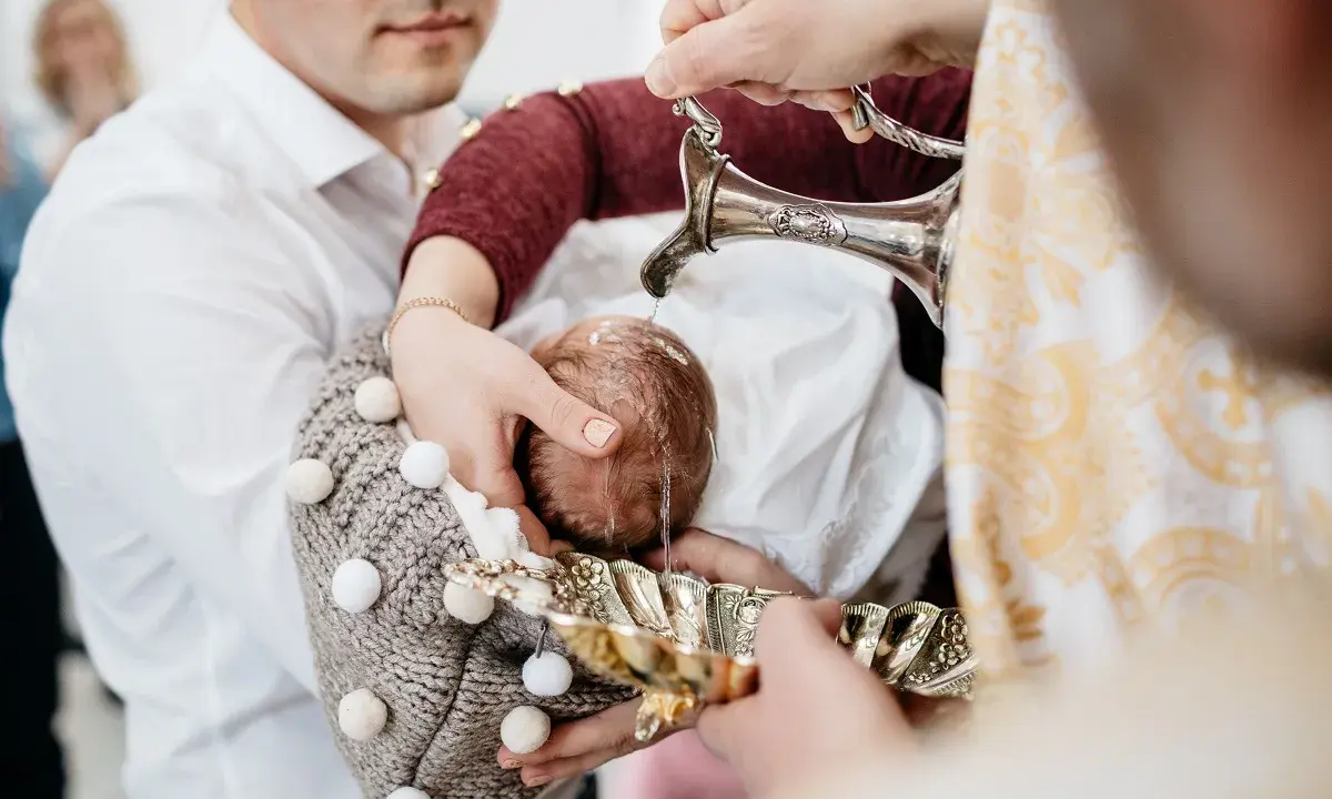 Woda święcona spływa na główkę dziecka podczas ceremonii na chrzcie.