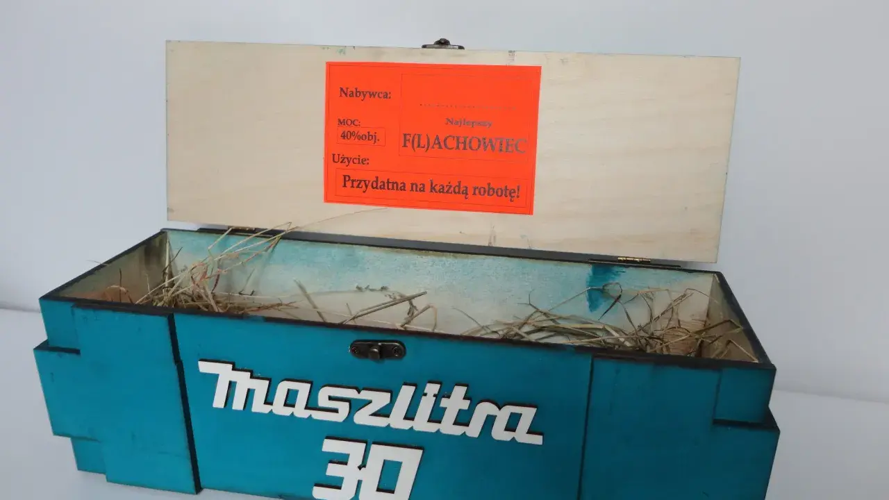 Otwarta, turkusowa skrzynka na 30 urodziny z napisem "Maszlitra 30". W środku sianko. Na wieczku etykieta "Najlepszy F(L)ACHOWIEC".