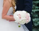 Piękny bukiet ślubny piwonie i eustoma w dłoniach pary młodej. Delikatne białe i różowe kwiaty tworzą romantyczną kompozycję.