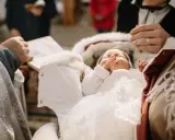Uroczysta chwila, kiedy chrzciny. Niemowlę w białej szatce spoczywa w ramionach bliskich, otoczone miłością i błogosławieństwem.