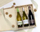 Eleganckie wino w skrzynce na prezent, idealne na wyjątkową okazję. Drewniana skrzynka z trzema butelkami wina, ozdobiona jutową wstążką i drewnianymi krążkami.