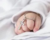 Dziecięca dłoń trzyma krzyżyk na łańcuszku, symbol tego, co jest potrzebne do chrztu.