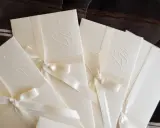 Eleganckie zaproszenia ślubne z monogramem, ozdobione satynową wstążką. Idealne, by dowiedzieć się, jak zrobić zaproszenie w Wordzie.