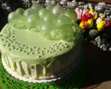 Zielony tort udekorowany koralikami i przezroczystymi, zielonymi balonami z żelatyny. Obok bukiet kolorowych tulipanów.