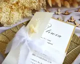 Elegancka papeteria na uroczystość: zaproszenie na Chrzest Święty z subtelnymi ozdobami, białymi wstążkami i suszonymi kwiatami.
