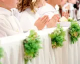 Dzieci w bieli podczas komunii, modlące się ręce. Dekoracje stołu z winogronami i zielenią, symbolizujące koszty komunii w kościele.