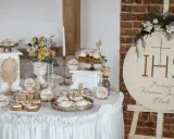 Stół z deserami na komunię w stylu boho: babeczki, makaroniki, torty. Drewniany napis IHS i "Pierwsza Komunia Święta".
