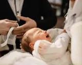Płacz dziecka podczas chrztu krok po kroku. Dziecko w białej szatce, trzymane przez rodziców.