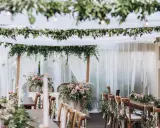 Uroczysty stół weselny w stylu boho, udekorowany kwiatami, zielenią i świecami.
