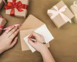 Piszę kartkę z podziękowaniem za zaproszenie na imprezę. Wokół leżą prezenty owinięte w papier i ozdobione wstążkami.