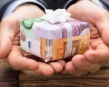 Dłonie trzymają prezent opakowany w banknoty euro. To pomysł, jak zapakować pieniądze na prezent dla dziecka, tworząc unikalną niespodziankę.