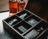 Elegancki zestaw z whisky w drewnianej skrzynce: dwie butelki, kieliszki z monogramem "A's", kamienie do whisky i podkładka.