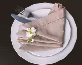 Eleganckie nakrycie stołu: jak złożyć serwetki na sztućce, ozdobione białą gałązką.