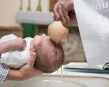 Chrzest dziecka. Kapłan polewa główkę niemowlęcia wodą święconą z muszli. To ważny moment, jak ile daje się na chrzciny.
