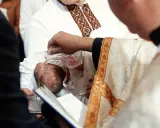 Chrzestni słuchają słów kapłana, gdy ten polewa wodą głowę niemowlęcia.