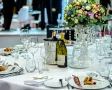 Elegancka dekoracja okrągłego stołu weselnego: kwiaty, wino, kieliszki i przystawki tworzą wykwintną atmosferę.