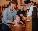 Chrzest dziecka w kościele. Ojciec trzyma niemowlę w miedzianej chrzcielnicy, a ksiądz polewa je wodą. To ważne chrzciny.