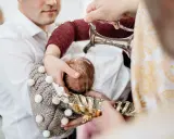 Woda święcona spływa na główkę dziecka podczas ceremonii na chrzcie.