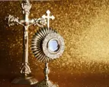 Monstrancja i krzyż na złotym tle. IHS to symbol Jezusa, który jest obecny w Eucharystii.