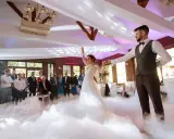Para młoda tańczy w chmurach dymu podczas wesela. Goście obserwują ich pierwszy taniec.