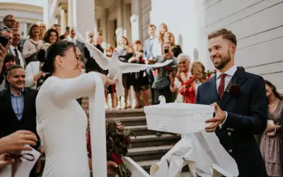 Para młoda wypuszcza gołębie na kameralnym weselu. W tle widać gości z telefonami.