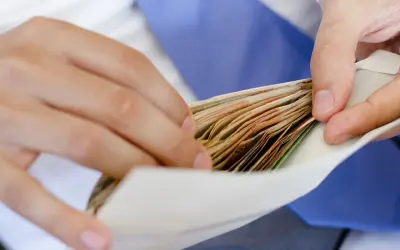 Dłonie wkładają plik banknotów do koperty na wesele.