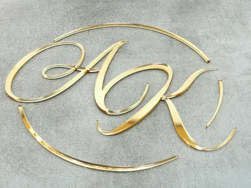Eleganckie, złote litery "AK" na szarym tle. Błyszczące, lustrzane litery tworzą inicjały, jakby wycięte z drogiego metalu.