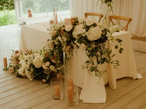Elegancki stół pary młodej ozdobiony bujną wiązanką kwiatów i świecami.