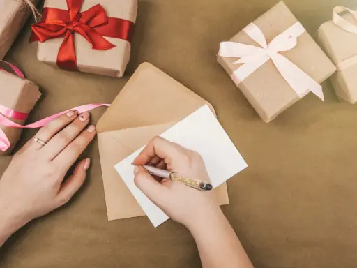 Piszę kartkę z podziękowaniem za zaproszenie na imprezę. Wokół leżą prezenty owinięte w papier i ozdobione wstążkami.