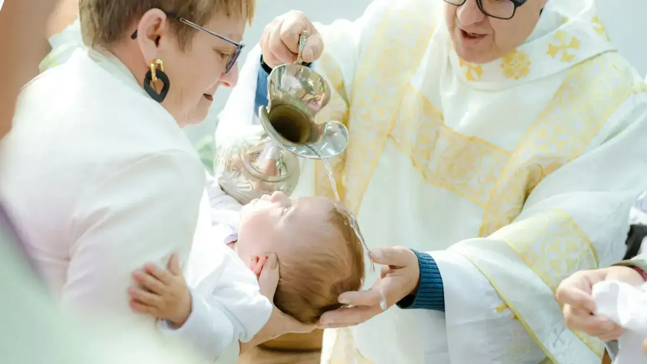 Chrzest dziecka. Kapłan polewa gł&oacute;wkę malucha wodą święconą. Warto wiedzieć, ile za chrzest zapłacimy.