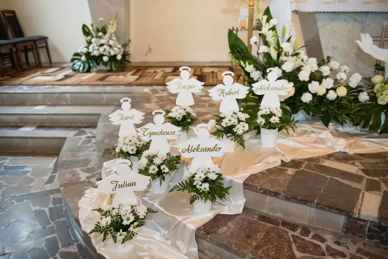 Urocze pomysły na dekoracje komunijne w kościele: aniołki z imionami dzieci i białe kwiaty.