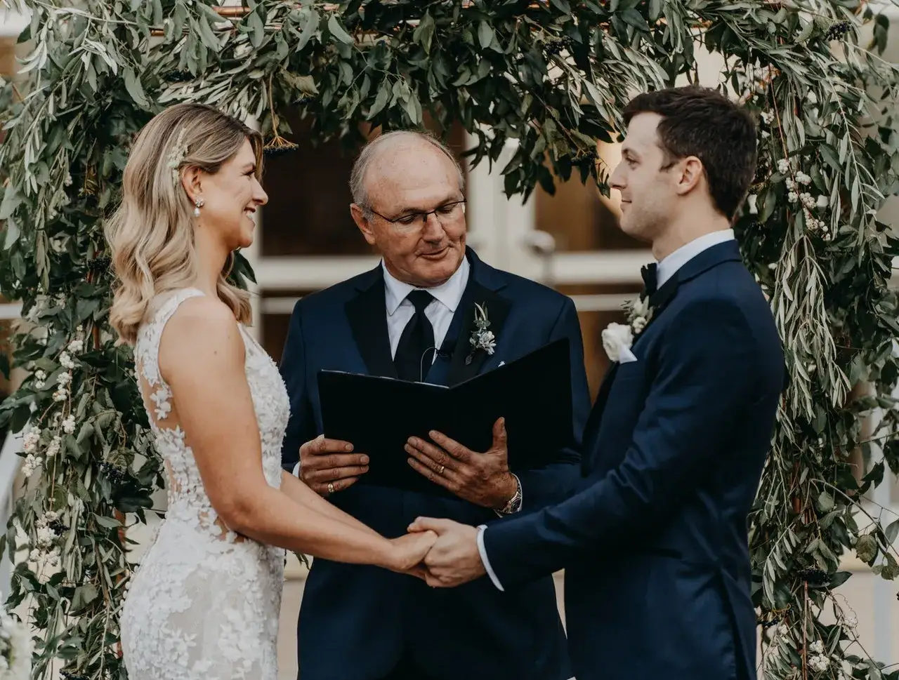Para młoda trzyma się za ręce podczas ceremonii. Przysięga małżeńska cywilna odbywa się pod łukiem z zieleni.