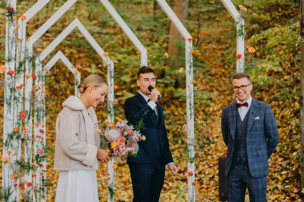 Piękna panna młoda z bukietem, pan młody przemawia do mikrofonu, a pan młody z uśmiechem. Wesele jesienią w otoczeniu kolorowych liści.