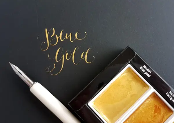 Złoty napis "Blue Gold" obok pióra i palety farb.